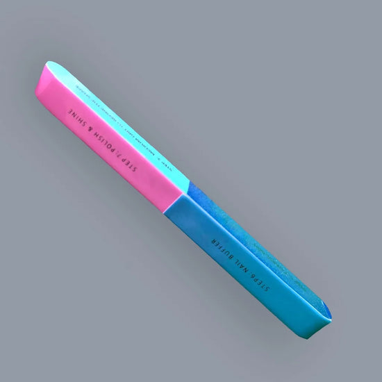 Full length angled view of de blinkie 7-in-1 nail buffer showing pink and blue sides against a grey background
