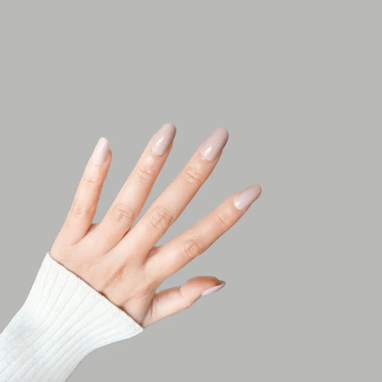 Fingers up pose showing de blinkie Bare Elegance soft pastel pink nude gloss press-on nails in short oval against a grey background with a white ribbed knit sleeve