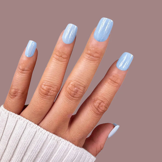 Spread hand showing de blinkie Bluebell Dream baby blue short square press-on nails against mauve background with white knit sleeve