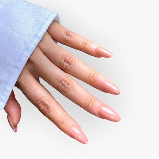 Downward spread hand showing de blinkie Blush Apricot warm peachy nude press-on nails in short almond shape against white background with light blue sleeve