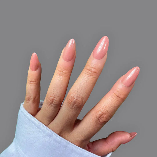 Upright open hand pose showing de blinkie Blush Apricot warm peachy nude press-on nails in short almond shape against mid grey background with white sleeve