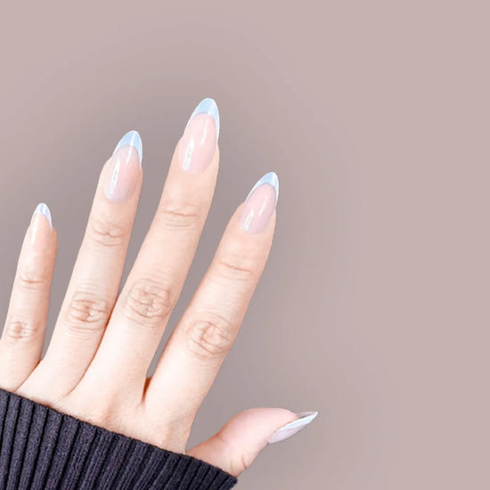 Fingers spread showing de blinkie Blush Mirage warm nude and aurora iridescent French tip press-on nails in short almond against a warm taupe background with a black ribbed knit sleeve
