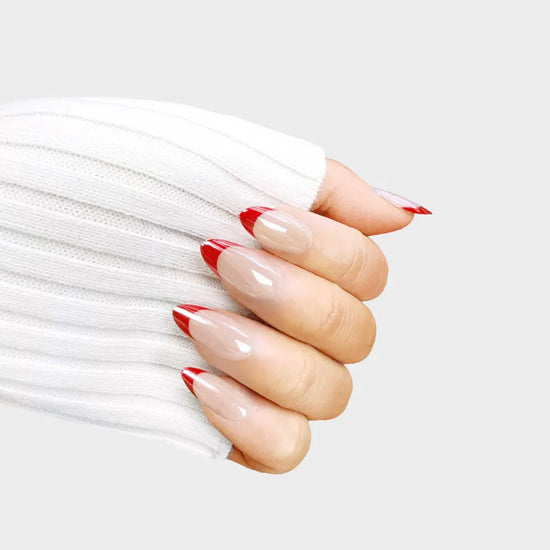 Horizontal close-up of de blinkie Boss Babe Red sheer nude press-on nails with crimson red French tips in short almond shape