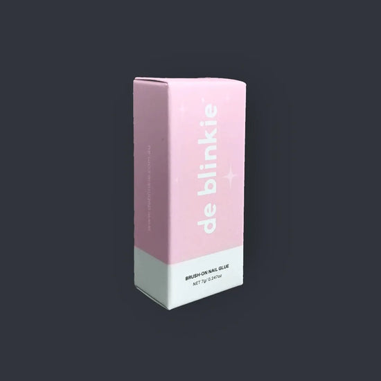 Angled view of de blinkie Brush-On Nail Glue 7g box showing brand name and product details against a dark background