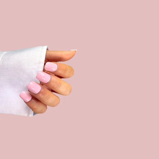 Close-up hand pose showing de blinkie Bubblegum Pop bright candy pink soft gloss extra short squoval press-on nails against blush pink background with white sleeve