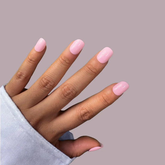 Diagonal spread hand showing Bubblegum Pop vibrant candy pink extra short squoval press-on nails against mauve background with light blue sleeve