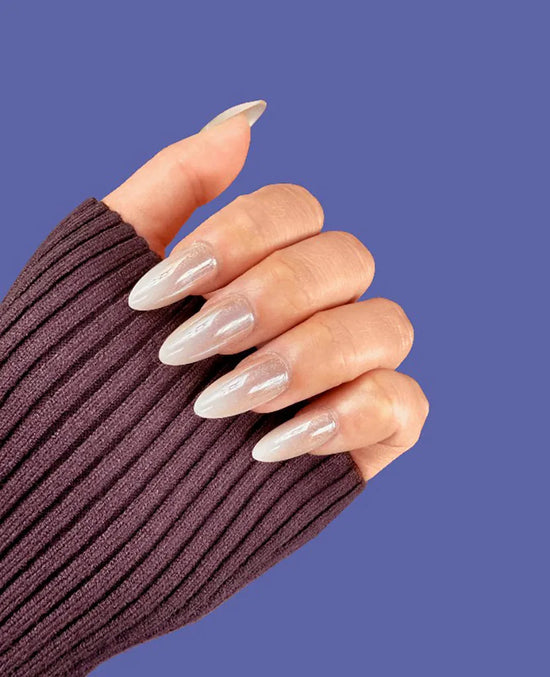 Claw pose showing de blinkie Champagne Veil champagne gold glazed ombre press-on nails in medium almond shape against blue background with dark ribbed knit sleeve