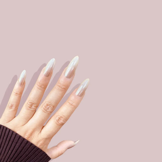 Fingers spread pose showing de blinkie Champagne Veil champagne gold glazed ombre press-on nails in medium almond shape against pink background with dark ribbed knit sleeve