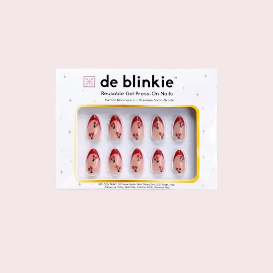 Product box shot showing de blinkie Cherry Blush sheer nude with cherry 3D detail and red glitter tips short almond press-on nails against pink background