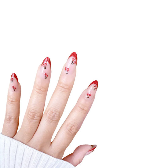 Fingers up pose showing de blinkie Cherry Blush sheer nude with cherry 3D detail and red glitter tips press-on nails in short almond shape against white background with white ribbed knit sleeve