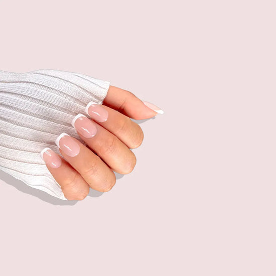 Claw pose showing de blinkie Chic Classique soft blush nude and white French tip press-on nails in extra short square against a blush pink background with a ribbed white knit sleeve