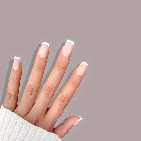 Spread hand showing de blinkie Chic Classique soft blush nude and white French tip press-on nails in extra short square against a warm grey background with a white ribbed knit cuff