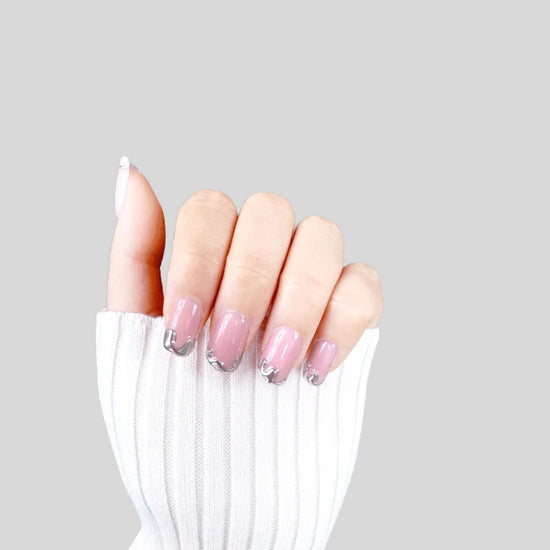 Claw pose showing de blinkie Chrome Whispers sheer blush pink with sculptural silver chrome tips in short square shape against grey background with white ribbed knit sleeve