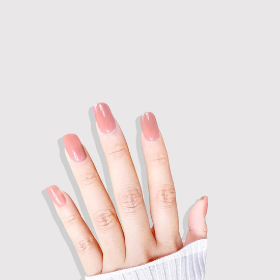 Diagonal downward spread hand showing de blinkie Cinnamon Glaze warm cinnamon rose press-on nails in short square against a soft light grey background with a white ribbed knit sleeve