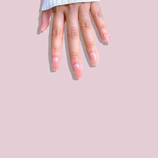 Downward spread hand showing de blinkie Cinnamon Glaze warm cinnamon rose press-on nails in short square against a soft pink background with a white ribbed knit sleeve