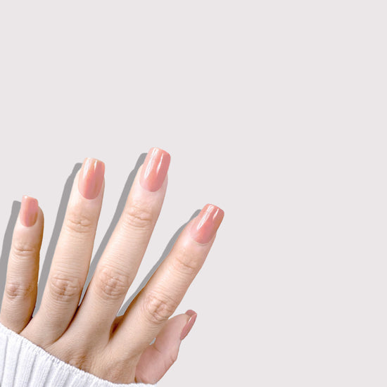 Upward hand pose showing de blinkie Cinnamon Glaze warm cinnamon rose press-on nails in short square against a soft grey background