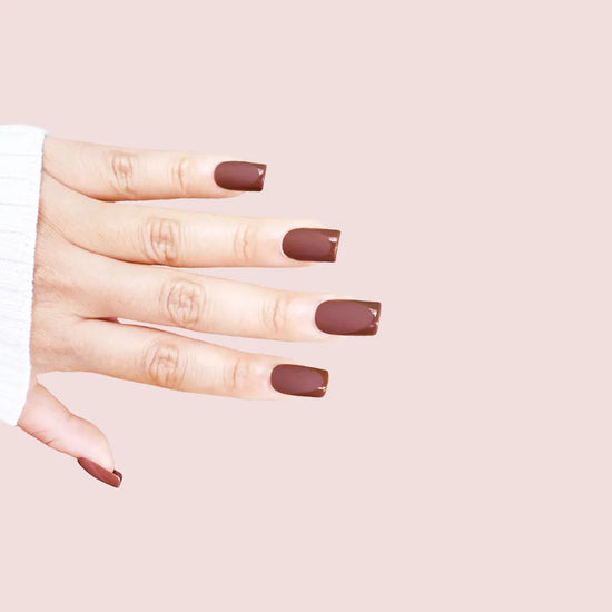 Diagonal hand pose showing de blinkie Cocoa Suede rich chestnut velvet matte press-on nails in medium square shape against pink background with white ribbed knit sleeve