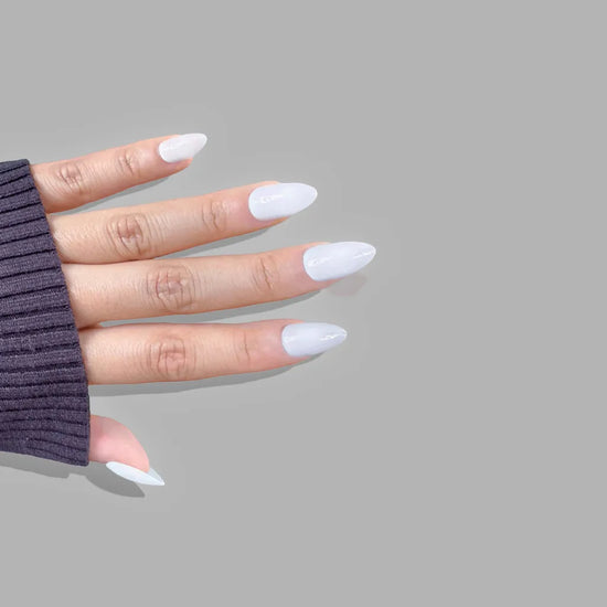 Diagonal spread hand showing de blinkie Creme Glacée clean crisp white press-on nails in short almond against a soft grey background with a purple ribbed knit sleeve