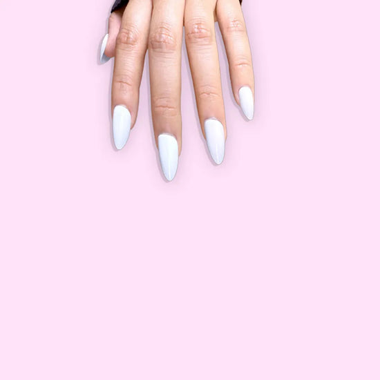 Horizontal spread hand showing de blinkie Creme Glacée clean crisp white press-on nails in short almond against a bright pink background with a dark navy ribbed knit sleeve