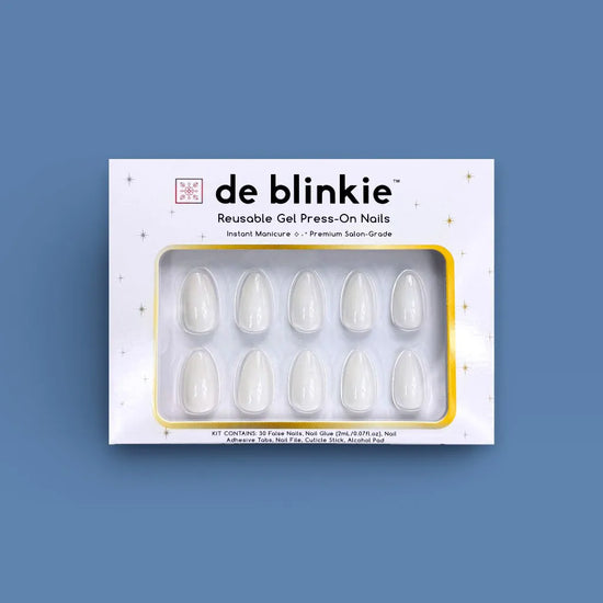 Product box shot of de blinkie Creme Glacée clean crisp white reusable gel press-on nails in short almond displayed in white branded packaging with gold star detailing against a dusty blue background