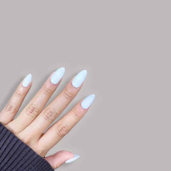 Spread hand showing de blinkie Creme Glacée clean crisp white press-on nails in short almond against a soft grey background with a dark grey ribbed knit sleeve