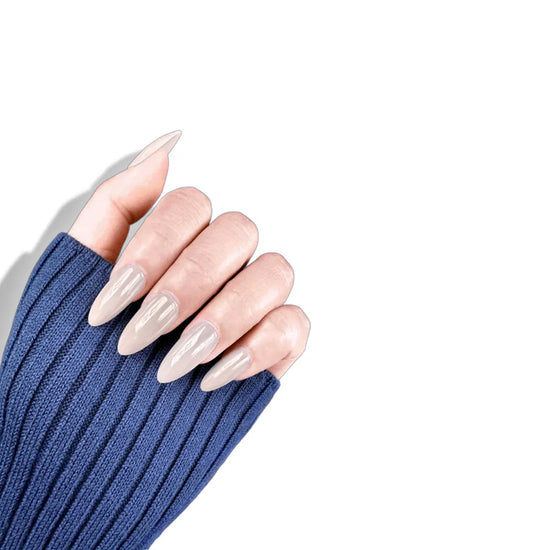 Claw pose showing de blinkie Creme Glazed sheer milky cream glazed press-on nails in medium almond against a white background with a navy ribbed knit sleeve