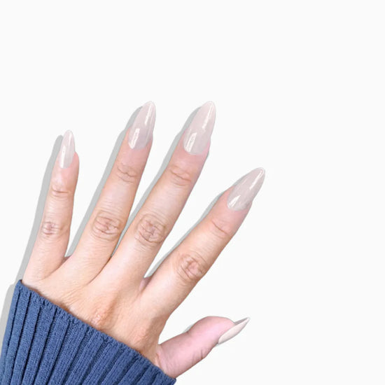 Fingers pointing upward showing de blinkie Creme Glazed sheer milky cream glazed press-on nails in medium almond against a white background with a navy ribbed knit sleeve