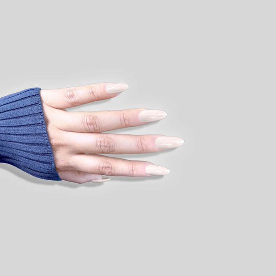 Spread hand showing de blinkie Creme Glazed sheer milky cream glazed press-on nails in medium almond against a soft grey background with a navy ribbed knit sleeve