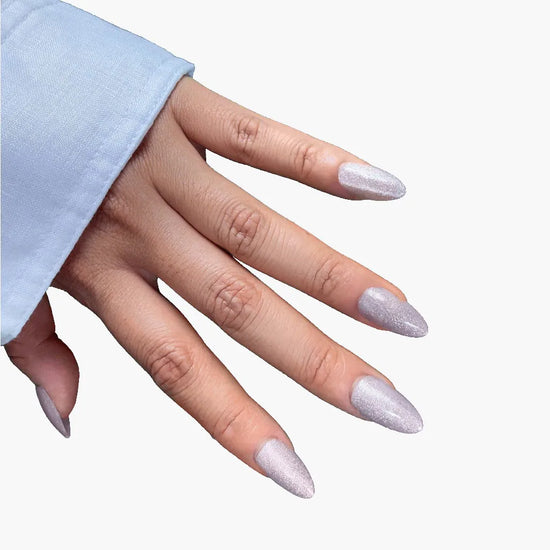 Downward diagonal hand view of Crystal Muse icy silver and lilac-grey shimmer short almond press-on nails with light blue sleeve