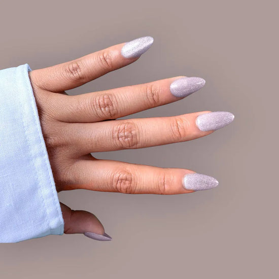 Horizontal spread hand showing Crystal Muse frosted icy silver shimmer short almond false nails against taupe background with light blue sleeve