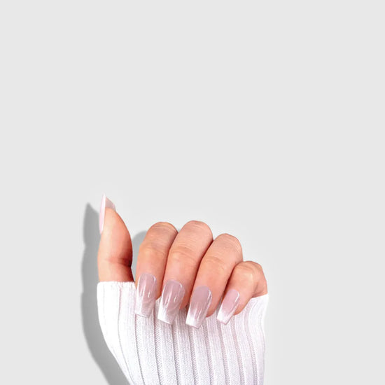 Claw pose showing de blinkie Frosted Beige nude pink frosted white press-on nails in short coffin against a light grey background with a white ribbed knit sleeve