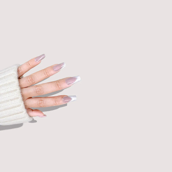 Diagonal downward hand showing de blinkie Frosted Beige nude pink frosted white press-on nails in short coffin against a warm white background with a white chunky knit sleeve