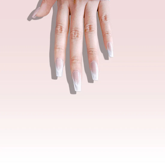 Fingers pointing downward showing de blinkie Frosted Beige nude pink frosted white press-on nails in short coffin against a soft blush pink gradient background
