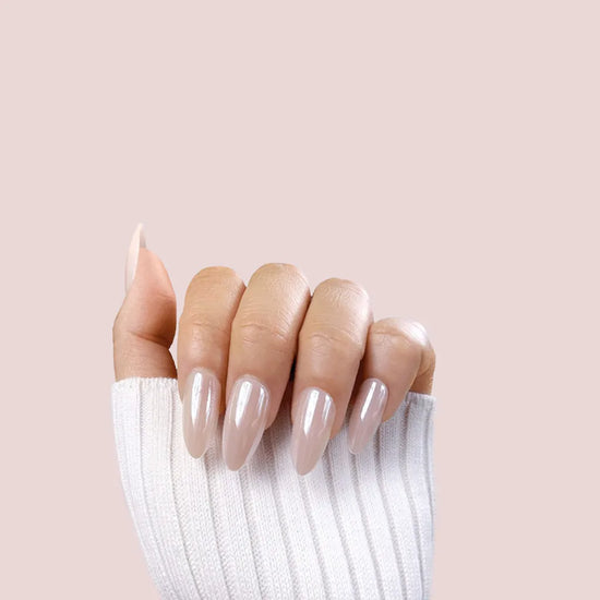 Claw pose showing de blinkie Glazed Hazel pearl chrome semi-sheer hazelnut nude medium almond press-on nails against blush pink background with white knit sleeve