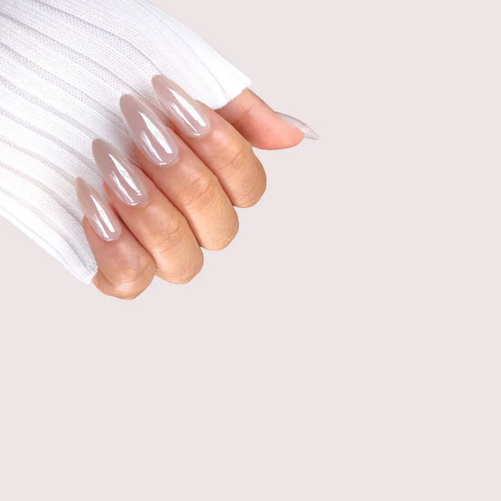 Diagonal hand position showing Glazed Hazel semi-sheer hazelnut nude pearl chrome medium almond press-on nails against blush pink background with white sleeve