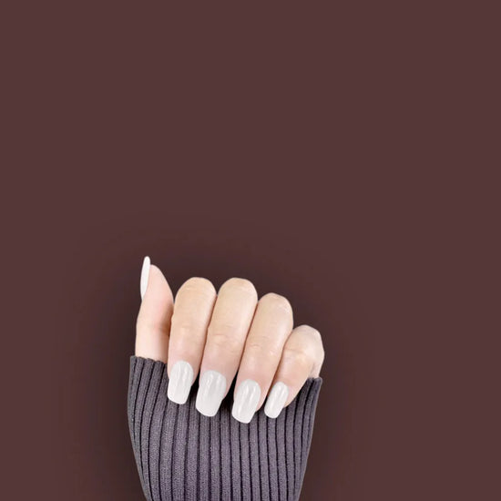 Claw pose showing de blinkie Glazed Milkyway milk white gloss press-on nails in short square against a deep burgundy background with a charcoal ribbed knit sleeve
