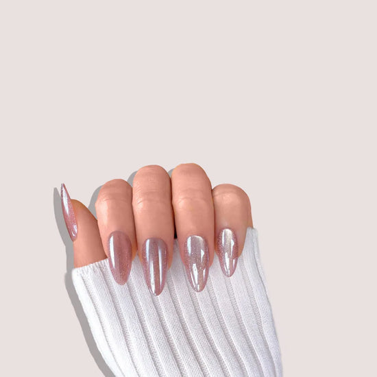 Claw pose showing de blinkie Glazed Mocha rosy mauve velvet cat eye shimmer short almond press-on nails against blush background with white knit sleeve