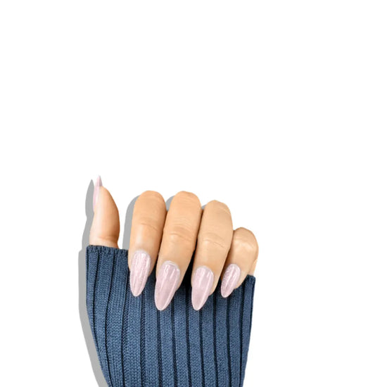 Diagonal upward hand pose showing de blinkie Glazed Rosé soft rose pink pearl shimmer short almond press-on nails against white background with navy knit sleeve