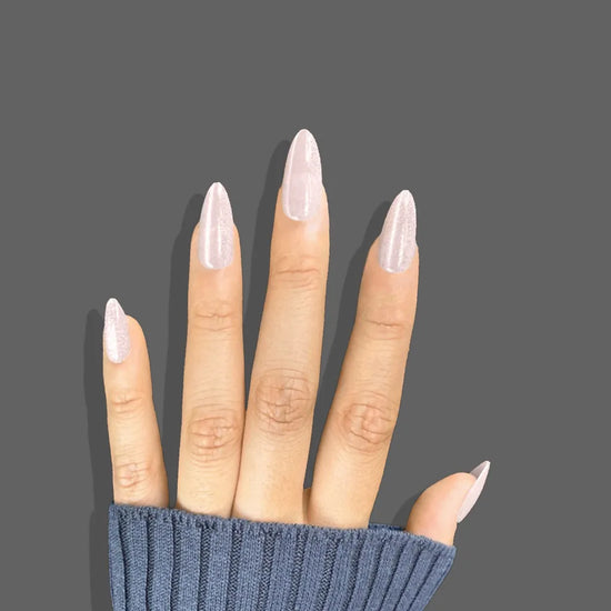 Upward hand pose showing de blinkie Glazed Rosé luminous rose pink pearl shimmer short almond false nails against grey background with navy knit sleeve