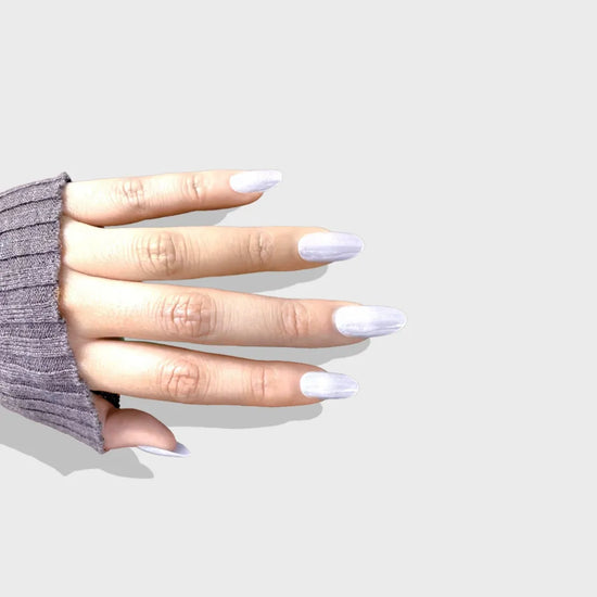 Down-facing hand pose showing de blinkie Glazed Stardust sheer pearl white icy shimmer press-on nails in medium oval shape against light grey background with dark grey ribbed sleeve