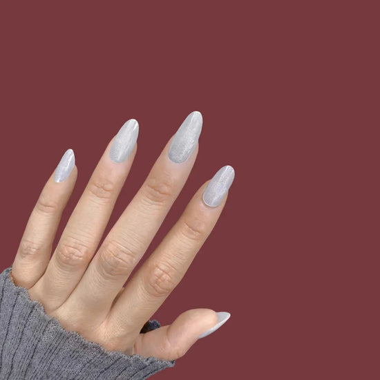 Spread hand showing de blinkie Glazed Stardust sheer pearl white opalescent shimmer press-on nails in medium oval shape against deep burgundy background with dark grey ribbed sleeve