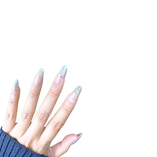 Spread hand showing de blinkie Glitter Drip sheer pink nude base with chunky multicolour glitter press-on nails in medium almond against a clean white background with a dark navy ribbed knit sleeve