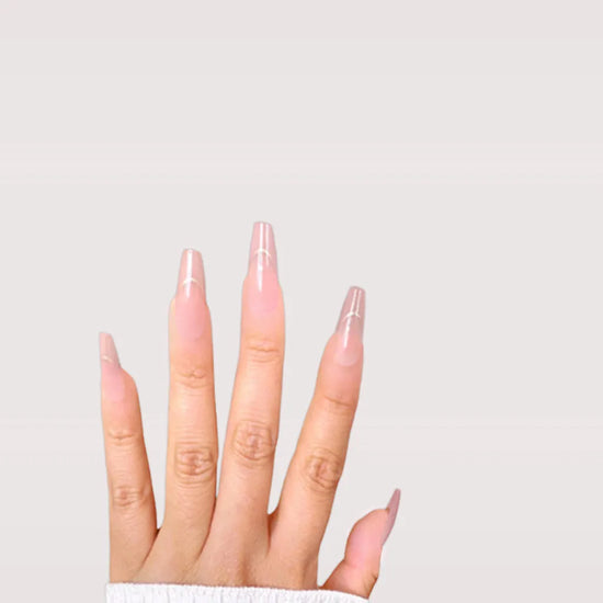 Fingers spread downward showing de blinkie Golden Grace sheer pink nude with gold trace press-on nails in long coffin against a warm grey background with a white ribbed knit sleeve