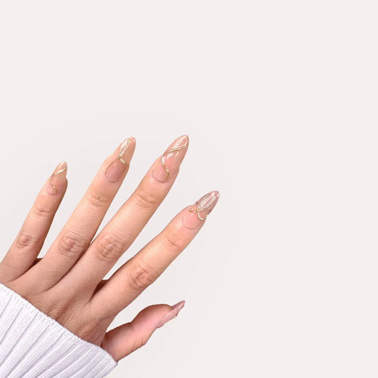 Fingers up pose showing de blinkie Golden Trace golden nude with 3D gold swirl detail press-on nails in medium almond shape against off-white background with white ribbed knit sleeve