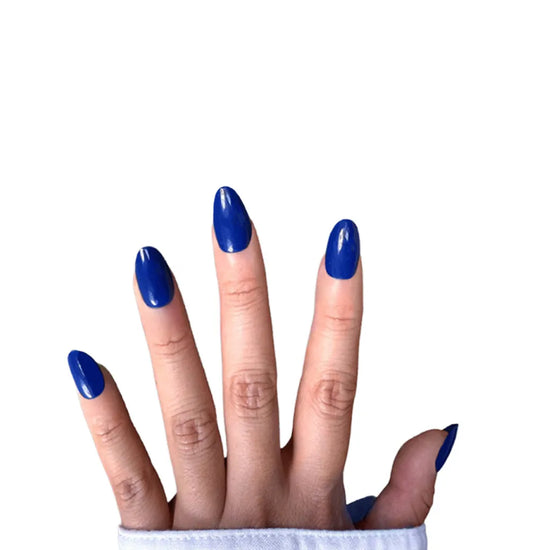 Spread hand showing de blinkie Indigo Ivy rich indigo blue press-on nails in short oval shape against white background with white denim sleeve