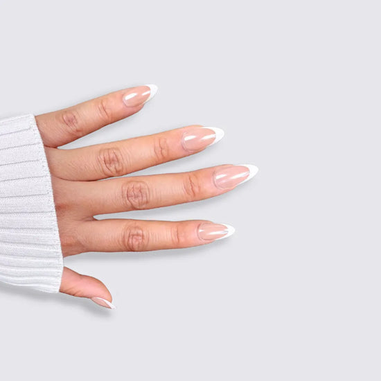 Side spread hand showing de blinkie Ivory Wave sheer nude and white French tip press-on nails in short almond against a light grey background with a white ribbed knit sleeve