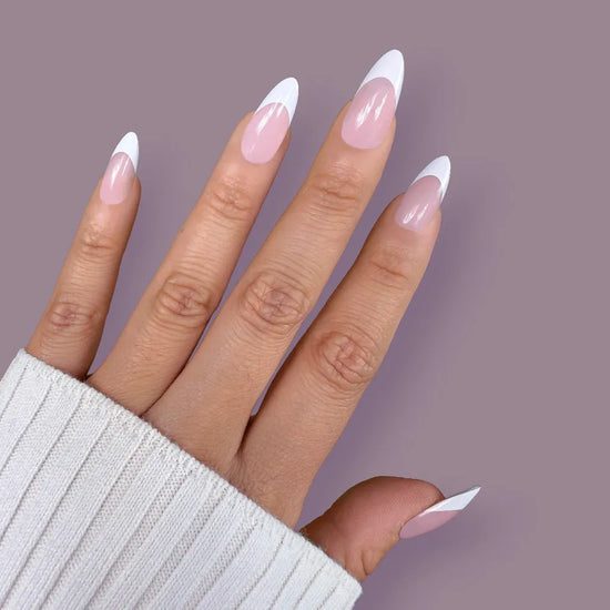 Fingers-up pose showing de blinkie Lady Primrose soft sheer pink base with bold white French tip press-on nails in medium almond shape against muted mauve background with white ribbed sleeve