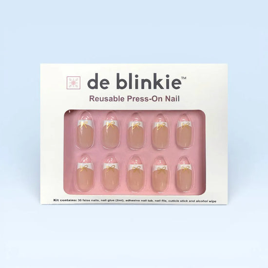 de blinkie Luxe Ribbon French reusable press-on nail kit box showing 10 short square false nails with sheer nude base, white French tips and gold bow nail art on pink tray against pale blue background