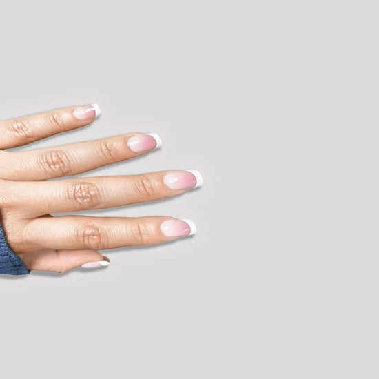 Downward spread hand alternate angle showing de blinkie Madame Grace sheer pink white French tip press-on nails in short square against a soft light grey background with a blue ribbed knit sleeve