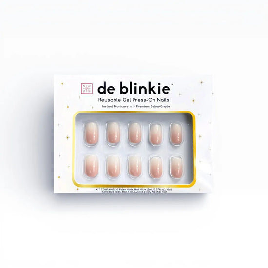 Product box shot of de blinkie Mademoiselle Glow soft peach nude to white ombre reusable gel press-on nails in short square displayed in white branded packaging with gold star detailing against a white background